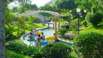 A swimming pool area with a wooden structure overhead, surrounded by lush greenery.