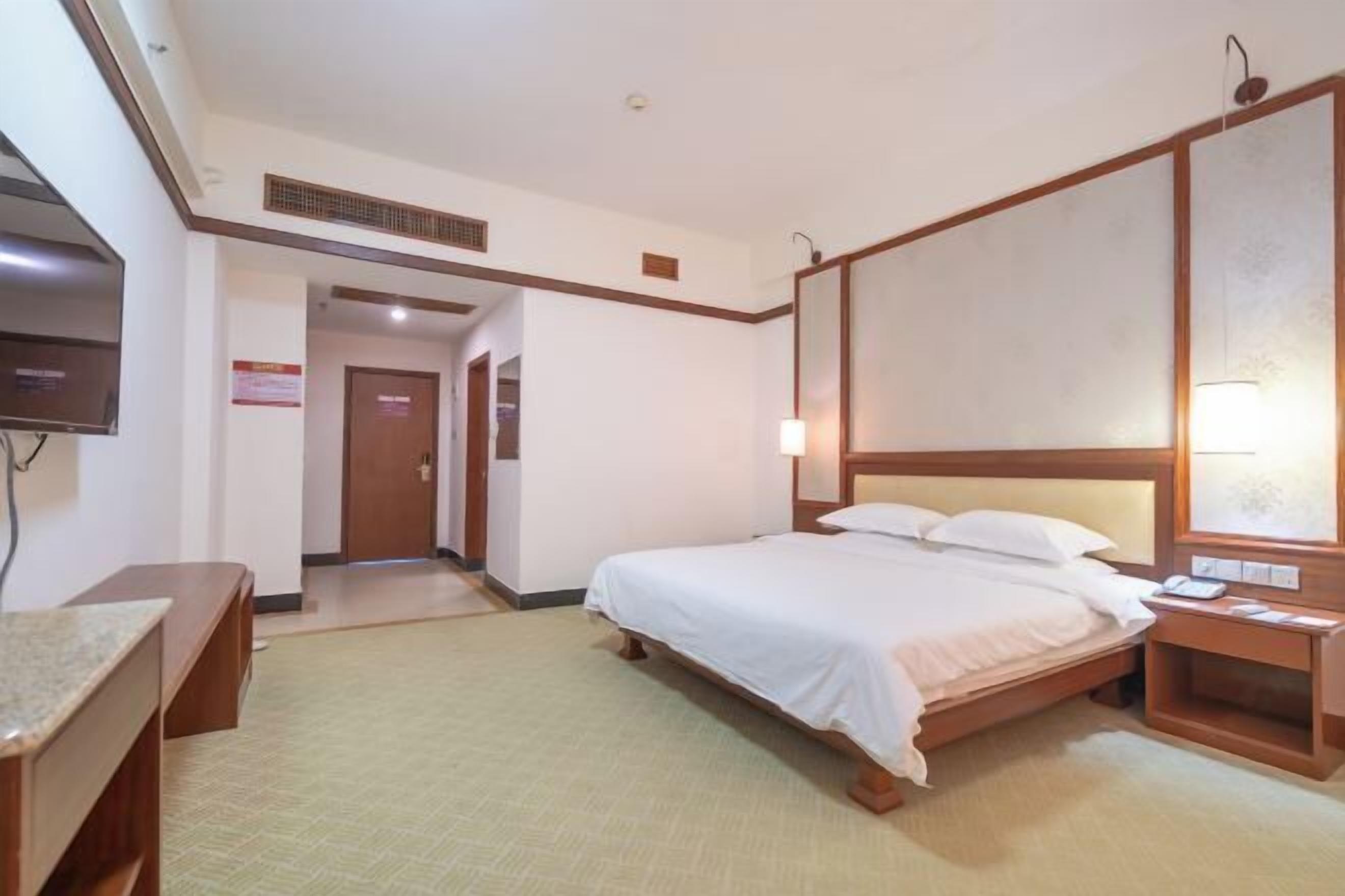 Hotellihuone, jossa on yksi sänky, yöpöytä, televisio ja puinen pääty.
