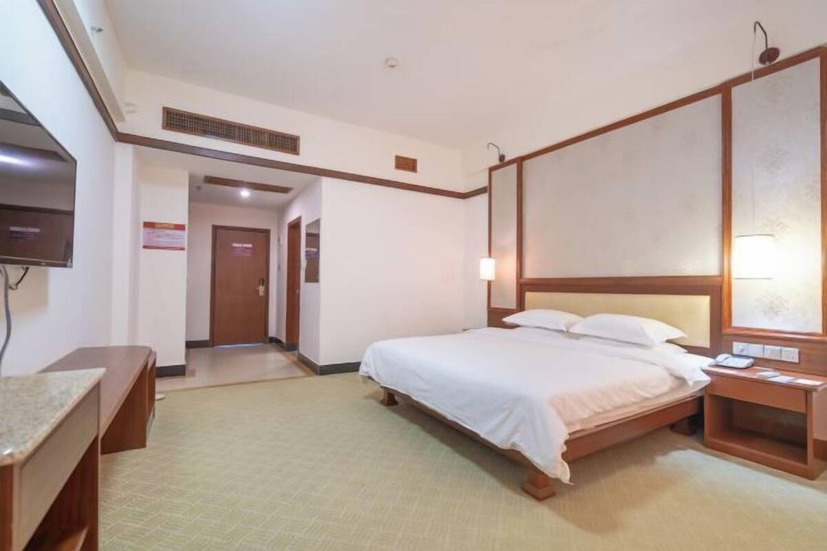 A hotel room with a single bed, a bedside table, a TV, and a wooden headboard.