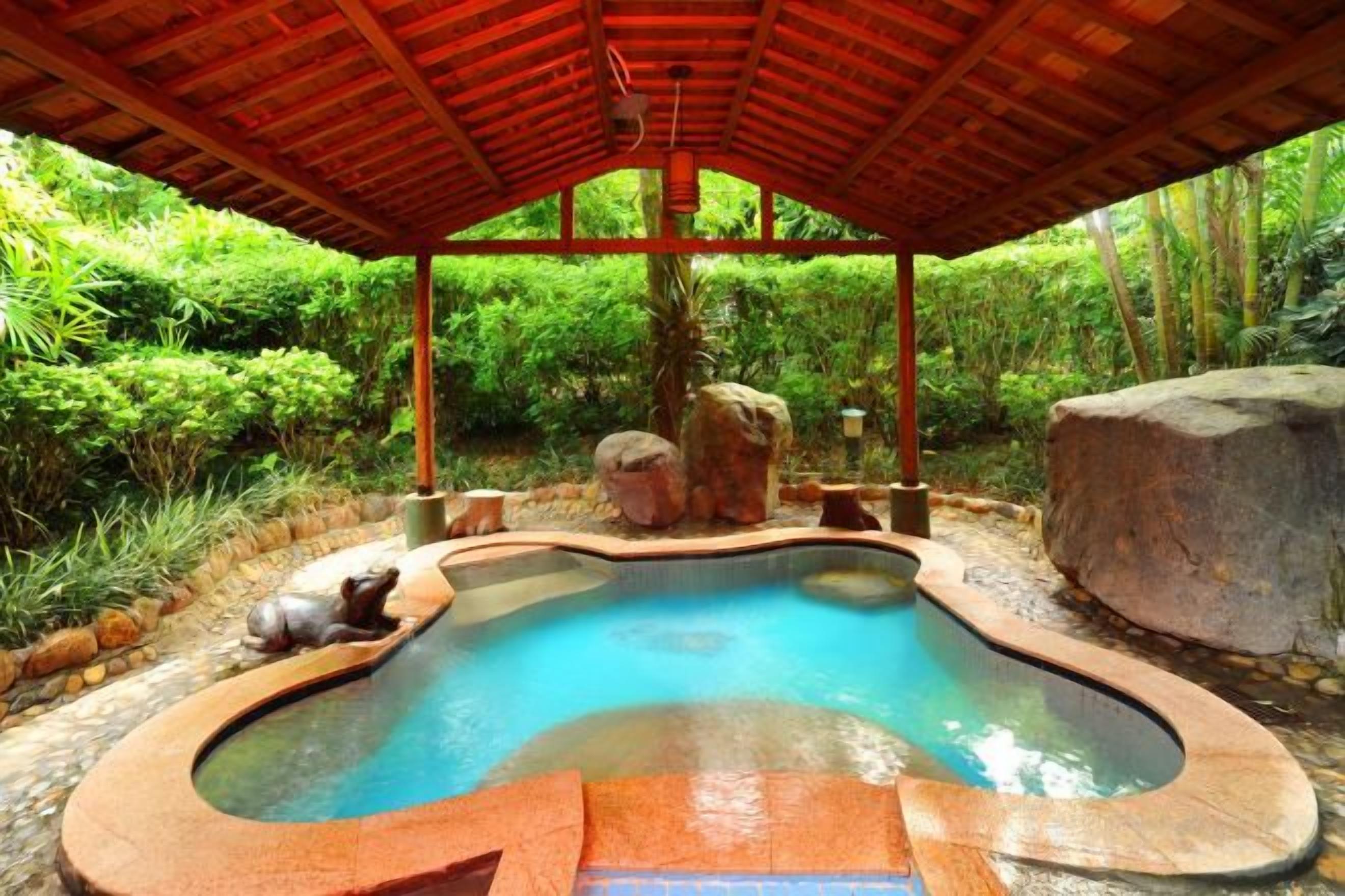 A hot tub under a wooden pergola surrounded by lush greenery.