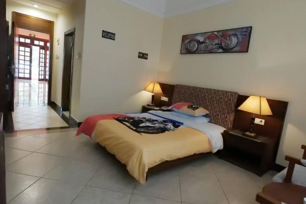 A hotel room with a bed, two bedside lamps, a headboard, a door, and a hallway.