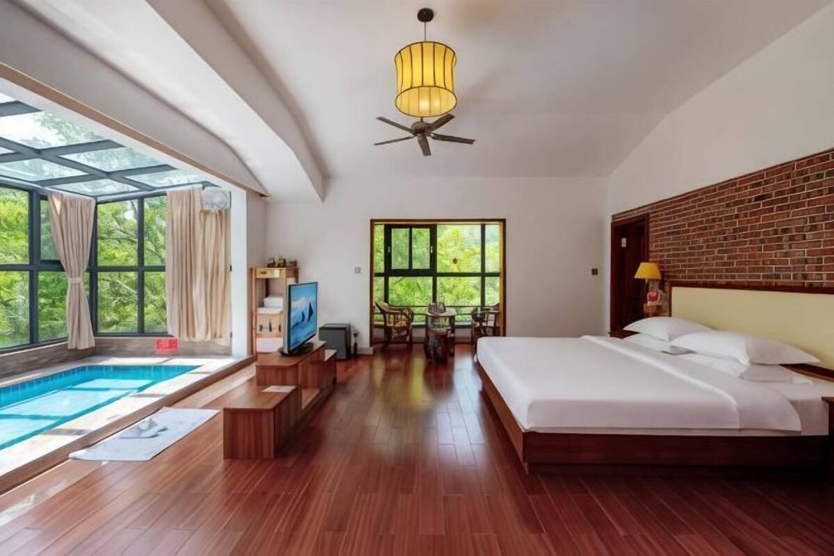A bedroom with a bed, a TV, a desk, and a window overlooking a pool.