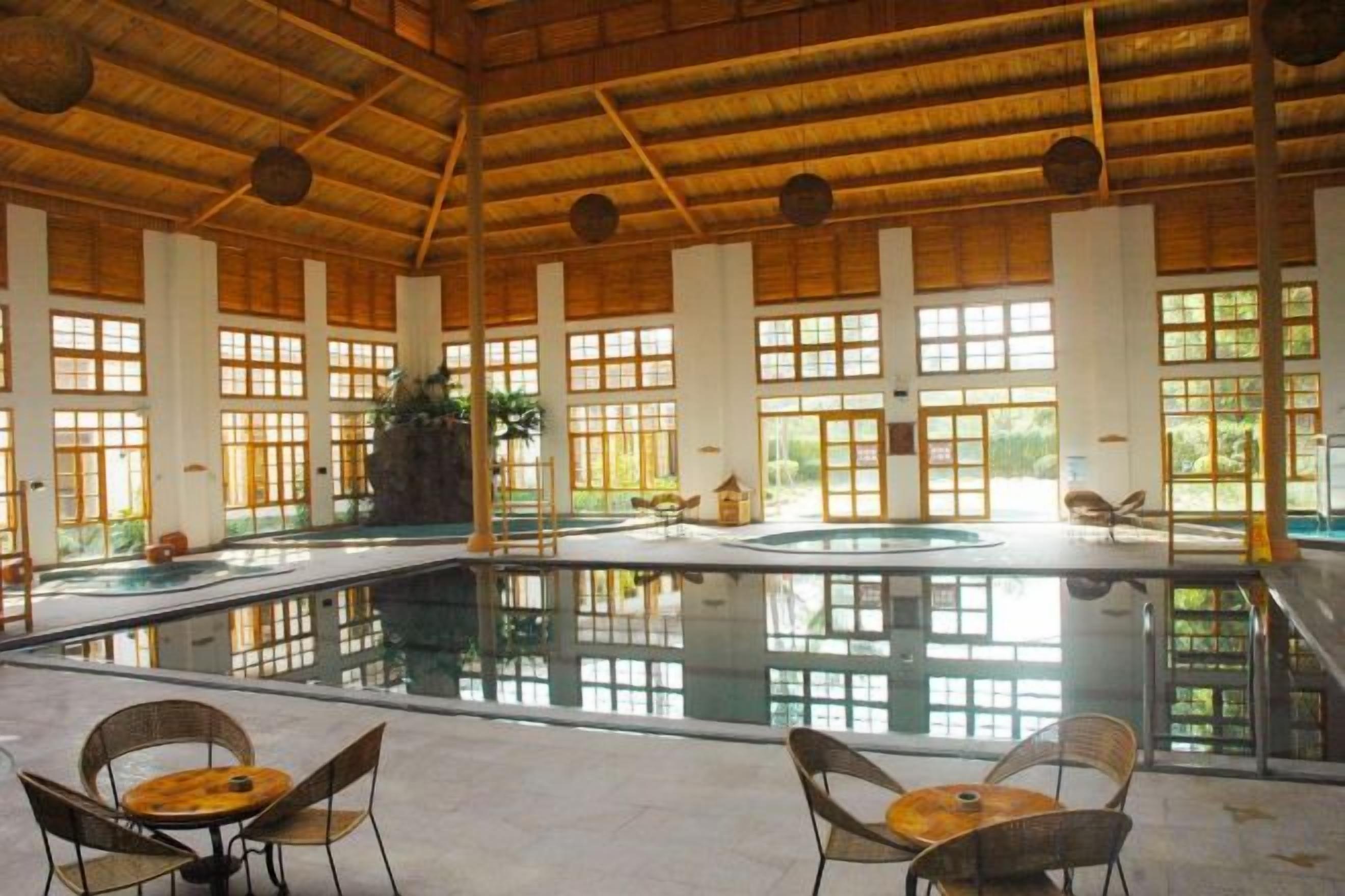 Une piscine intérieure dotée d’un toit de chaume, de grandes fenêtres et d’espaces aménagés pour se détendre.