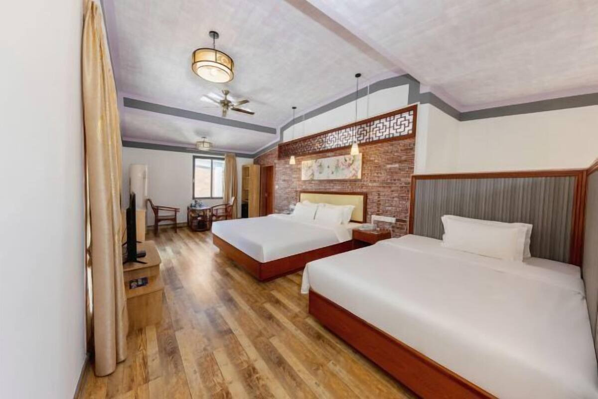A hotel room with two beds, a ceiling fan, a wooden floor, and a brick accent wall.