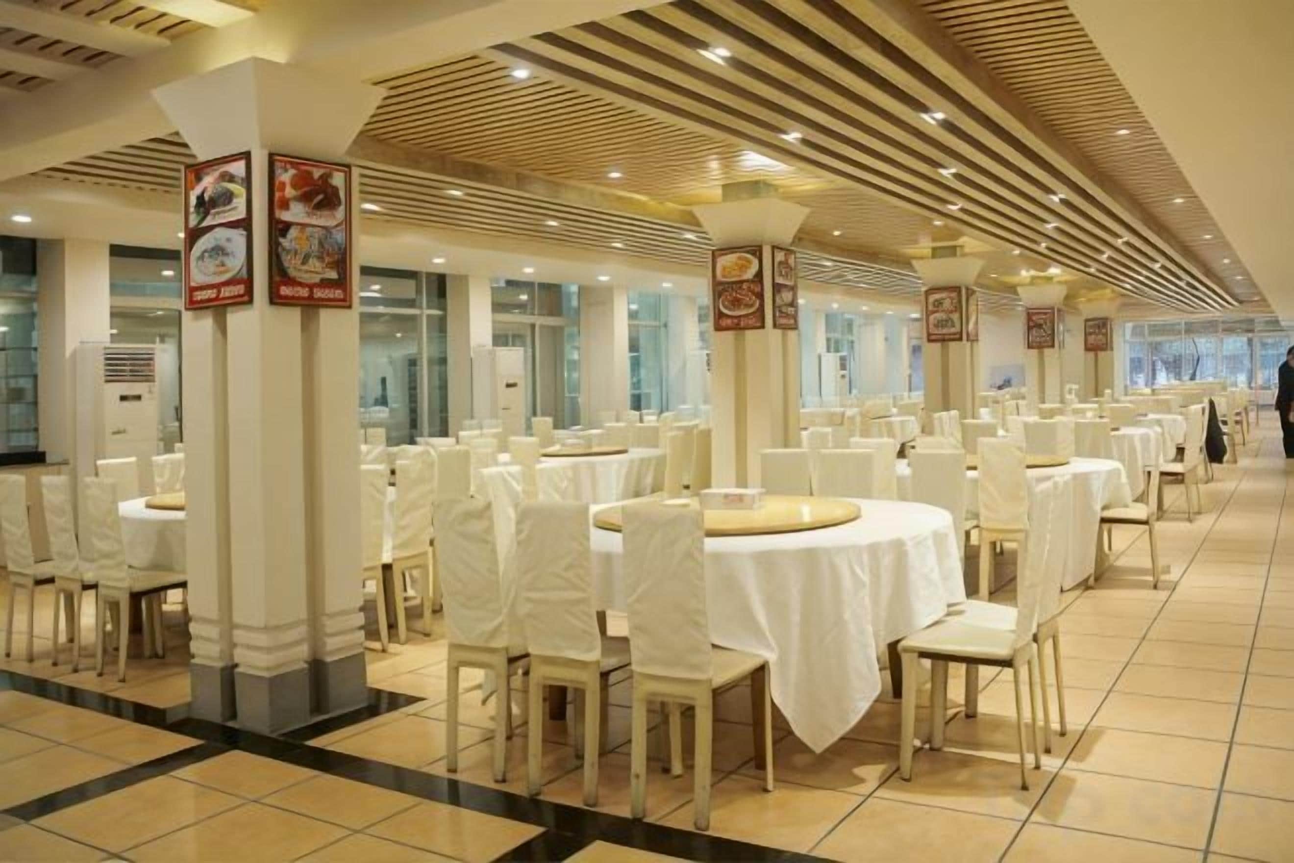 A banquet hall with round tables and chairs, white tablecloths, and columns with signage.