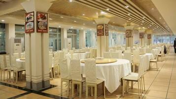 A banquet hall with round tables and chairs, white tablecloths, and columns with signage.