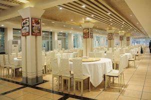 Un salón de banquetes con mesas redondas y sillas, manteles blancos y columnas con señalización.