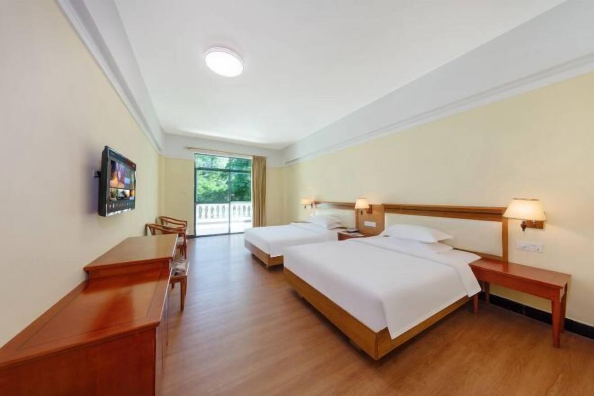 A hotel room with two beds, a desk, and a TV.