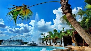 A pool area with a water fountain, palm trees, and a clear blue sky. - Enping Jinjiang Hotspring Hotel (Enping)