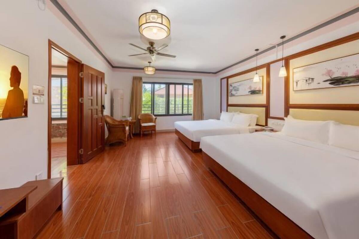 A hotel room with two beds, a ceiling fan, wooden flooring, and artwork on the walls.