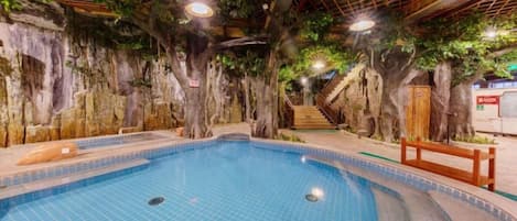 An indoor swimming pool with a tiled floor, surrounded by artificial rock walls and trees.