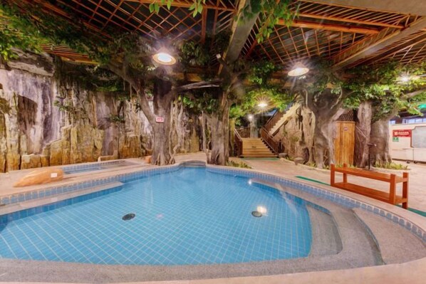 An indoor swimming pool with a tiled floor, surrounded by artificial rock walls and trees. - Enping Jinjiang Hotspring Hotel (Enping)
