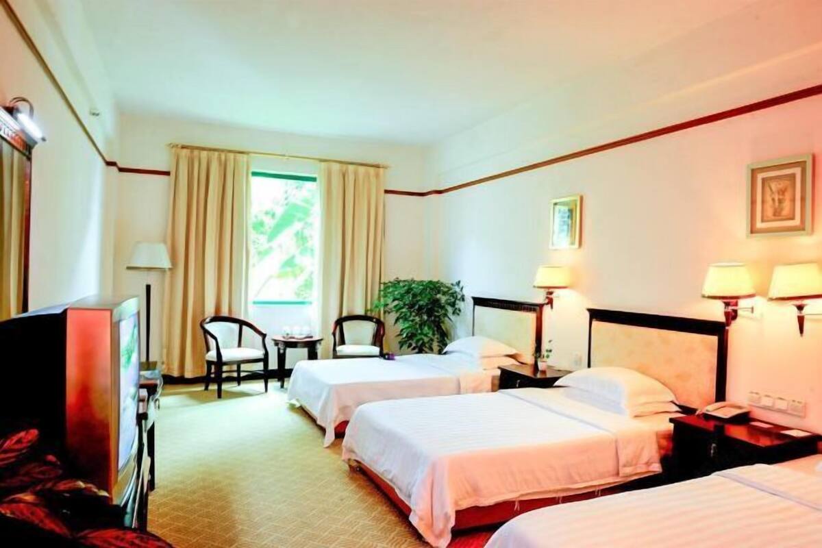 A hotel room with two beds, a TV, a desk, a chair, and a window with curtains.