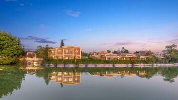 A multi-story building with a reflection in the water, surrounded by greenery.