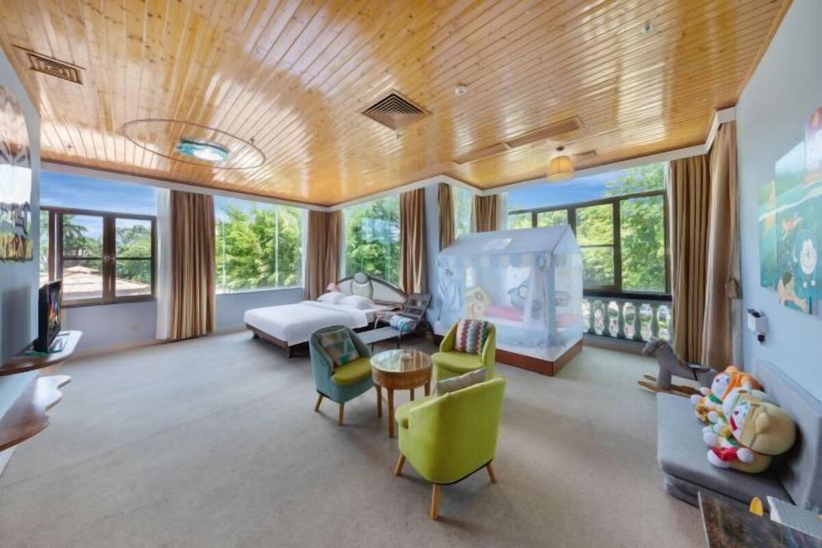 A spacious room with a wooden ceiling, large windows, a bed, a sofa, and a small table.
