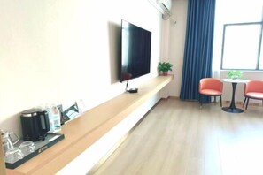 Camera d'albergo con televisore a schermo piatto montato a parete, un tavolino consolle in legno con una macchina per il caffè e bicchieri, due poltrone rosse attorno a un piccolo tavolo e una pianta in vaso.