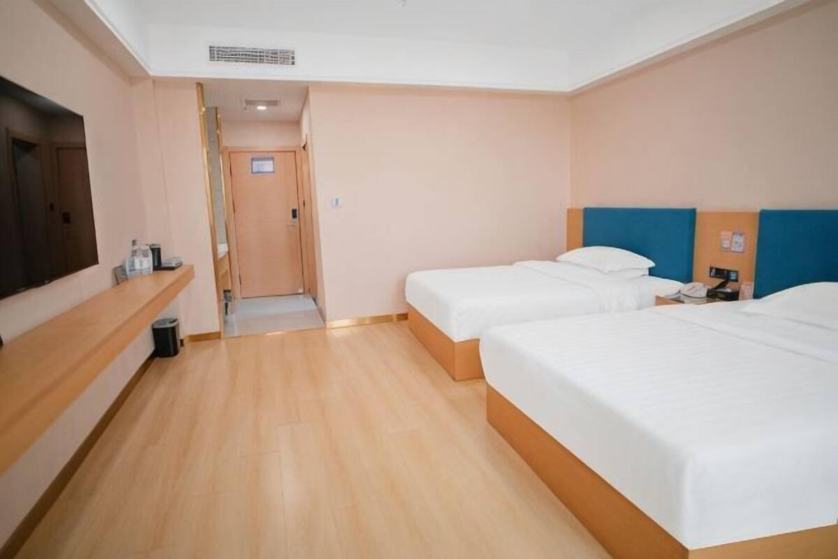 Habitación de hotel con dos camas, un televisor, un escritorio y una puerta que da a un pasillo.