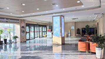 A hotel lobby with a reception desk, seating area, and potted plants.