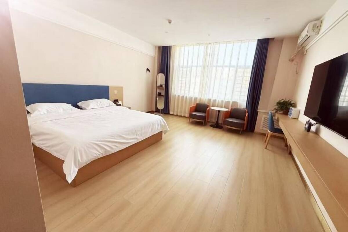Habitación de hotel con una cama grande, un escritorio, una silla, un televisor y una ventana con cortinas.