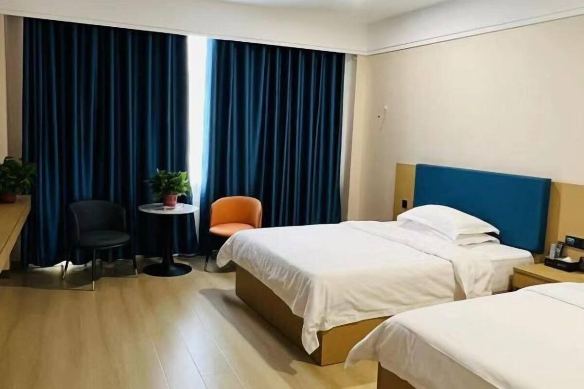 Habitación de hotel con dos camas, una mesita, una silla y una planta en maceta.