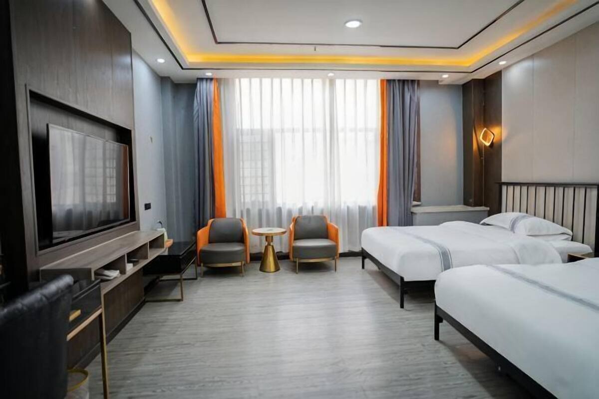 Una habitación de hotel con televisión, dos camas individuales, un sofá, un escritorio y una silla.