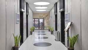 A modern hallway with circular light fixtures, potted plants, and a bookshelf. - Jiujiantang Yijin Hotel (Hangzhou)