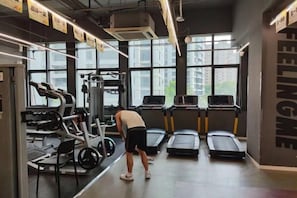 Een sportschool met loopbanden, krachttrainingsapparatuur en een groot raam.
