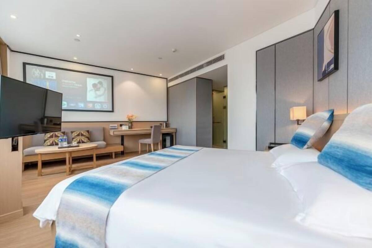 A modern hotel room with a large bed, a desk, a flat-screen TV, and a seating area with a sofa and chairs.