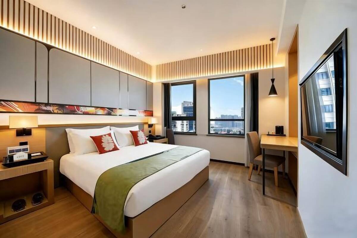 A modern hotel room with a large bed, a desk, and a view of the city.