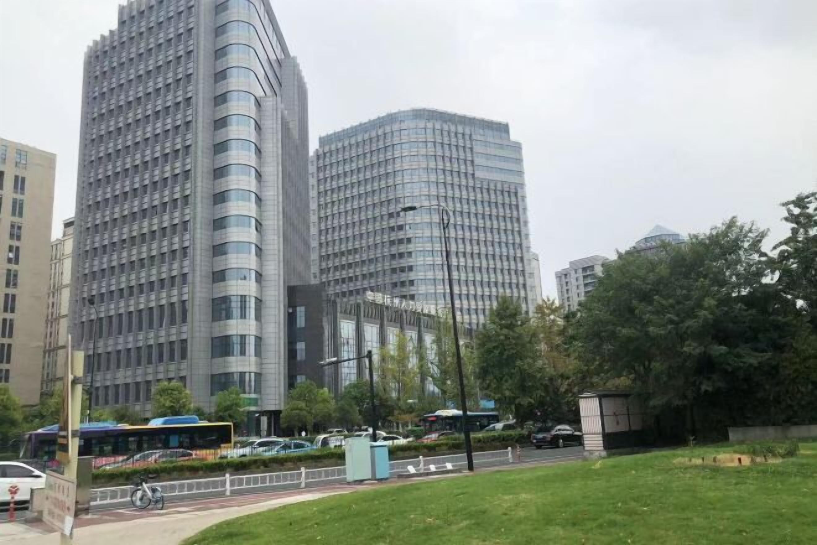 A modern urban area with tall buildings, a grassy park, and a bus stop.