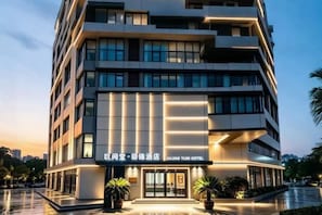 A multi-story hotel with a modern facade, illuminated signage, and potted plants at the entrance.