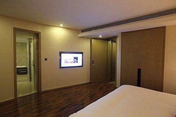 A hotel room with a large bed, a flat-screen TV mounted on the wall, and a wardrobe.