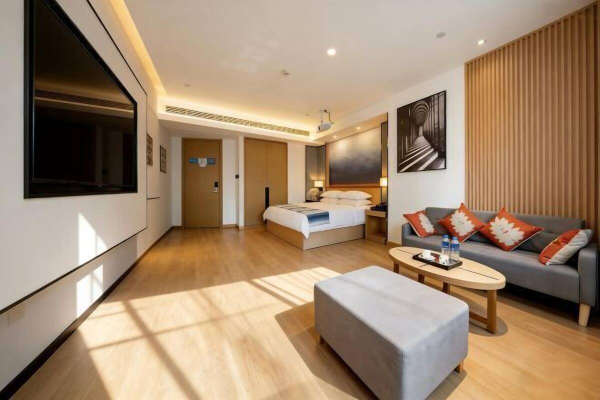 A modern hotel room with a large bed, a sofa, a coffee table, and a TV.