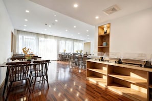 A spacious dining area with wooden flooring and multiple tables and chairs.