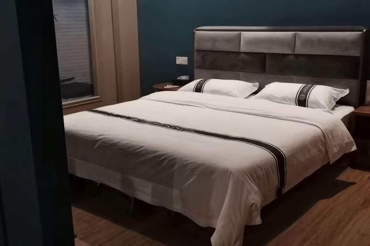 Ein ordentlich bezogenes Bett mit Kopfteil, Nachttisch und einem Fenster mit Jalousien.