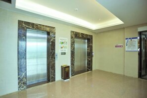 A hallway with two elevators, a trash bin, and a sign on the wall.
