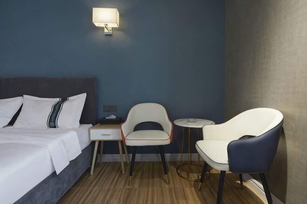 Une chambre d’hôtel comprenant un lit, deux chaises, une petite table, une table de chevet et une lampe fixée au mur.