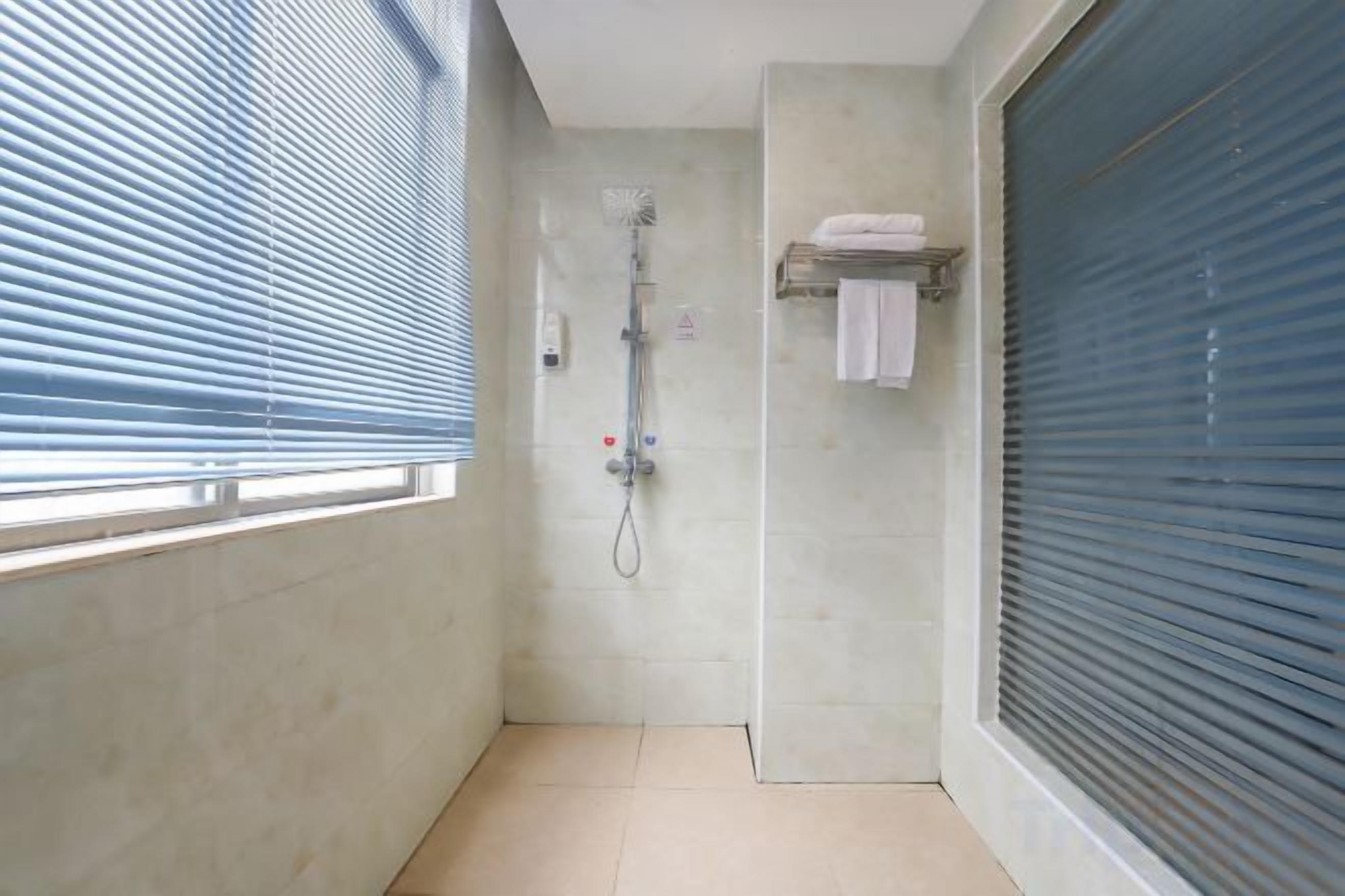 A narrow bathroom with a shower, a window with blinds, and a towel rack.