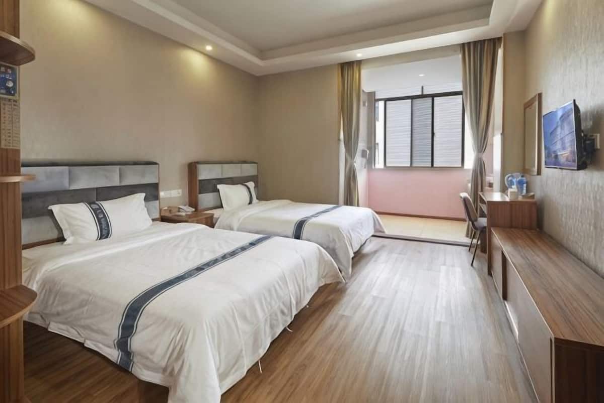Ein Hotelzimmer mit zwei Betten, einem Schreibtisch, einem Stuhl, einem Nachttisch und einem Fenster mit Vorhängen.