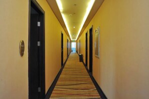 A hotel hallway with doors on both sides, a carpeted floor, and a long corridor leading to a bright area at the end. - Dongguan Tian Boutique Hotel (Dongguan)