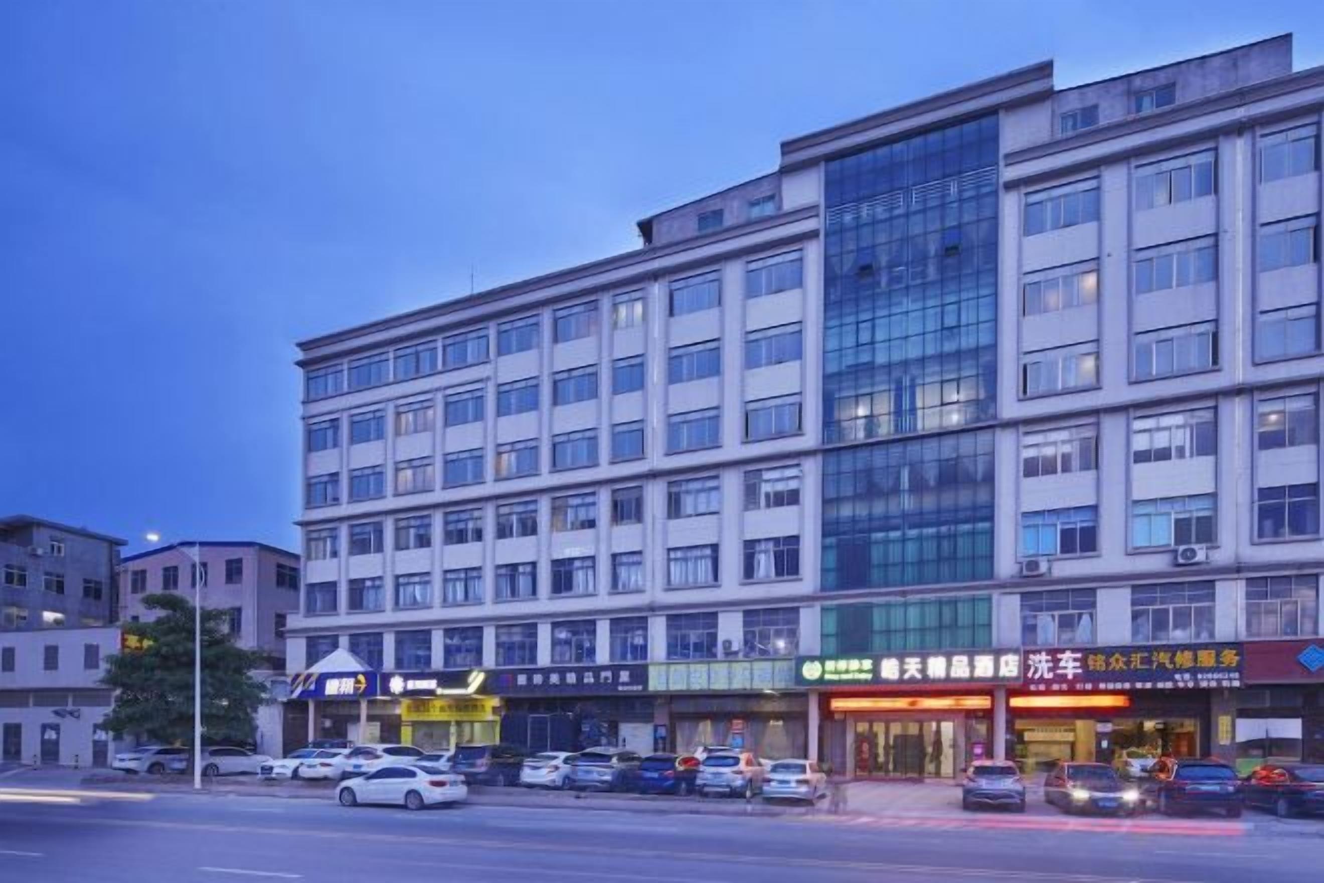 A multi-story building with a glass facade, several ground-level shops, and parked cars.