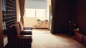 A room with a sofa, a desk, a chair, a window with curtains, and a view of the outside.