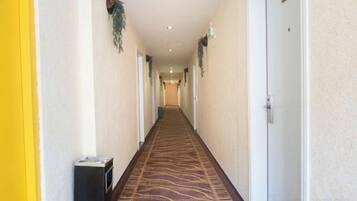 Corredor de hotel com piso revestido de carpete, portas em ambos os lados e uma lixeira à esquerda.