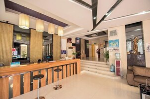 Un vestíbulo de hotel con mostrador de recepción, taburetes de bar, una escalera y un área de descanso.
