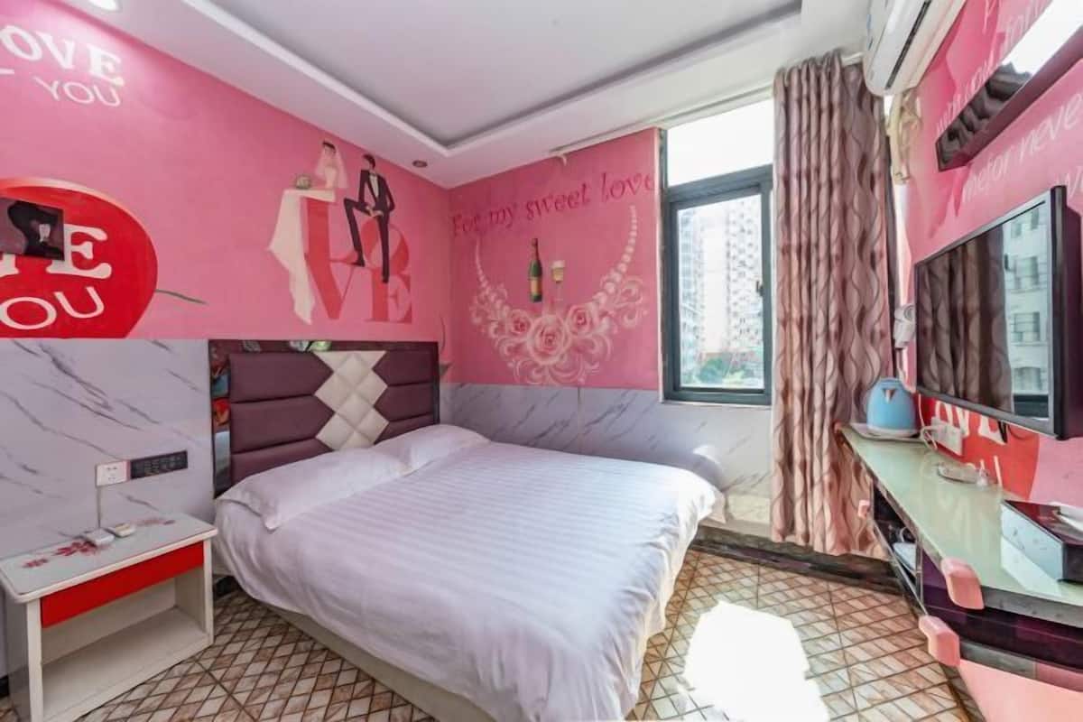 A bedroom with a bed, a nightstand, a TV, and a window with curtains.