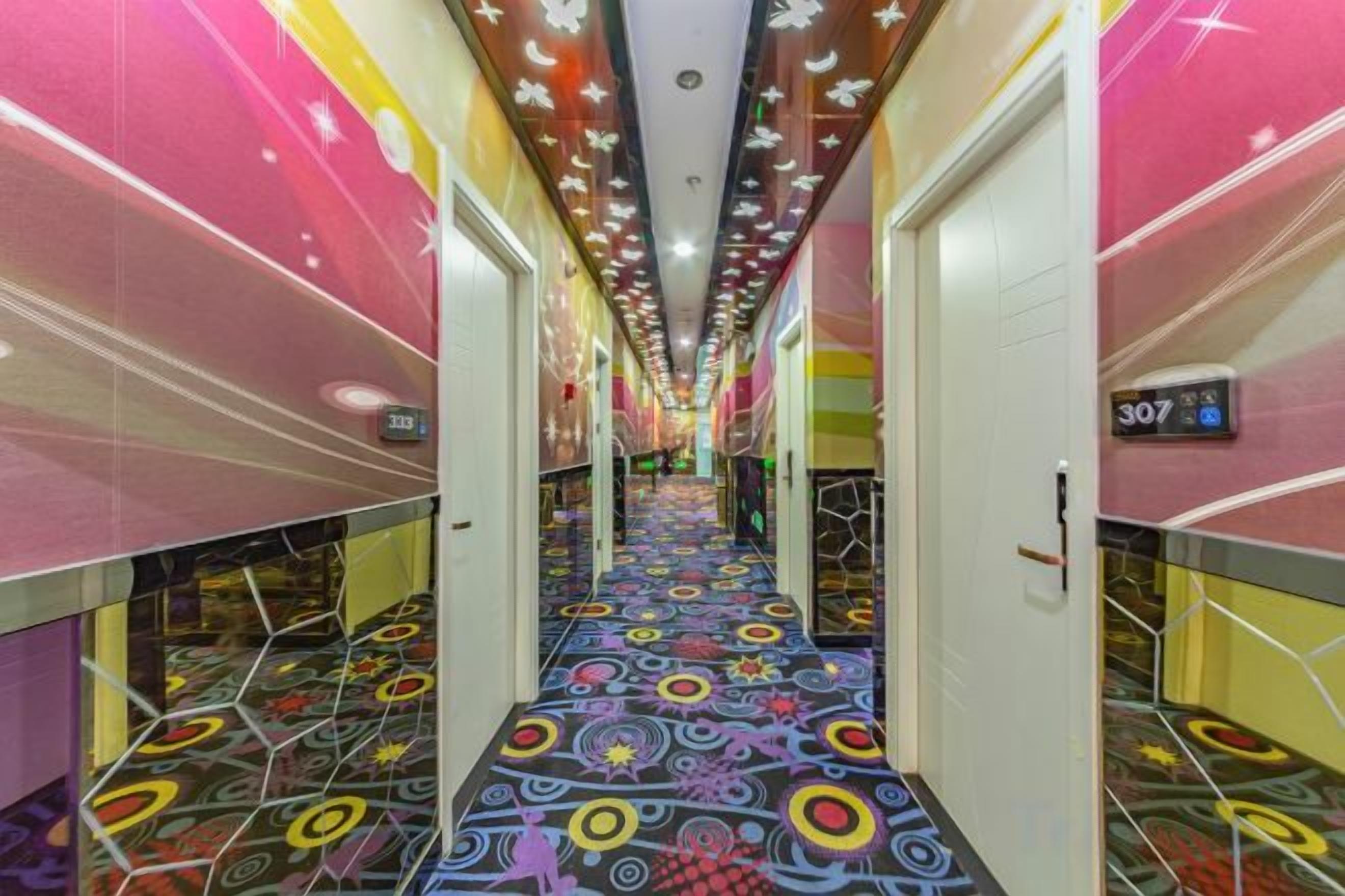 A brightly lit hallway with a colorful patterned floor, doors on both sides, and a number sign on the right wall.
