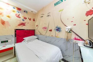 Un dormitorio con cama, cabecera roja, tocador con espejo y pared decorada con motivos florales y de corazón.