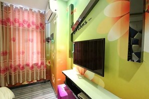 A room with a TV mounted on a wall, a bed, a window with curtains, and a wall with a colorful abstract design. - Shenli Hostel (Shanghai)