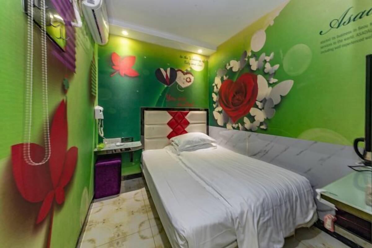 A small, brightly colored room with a bed, a desk, and a wall with floral and butterfly decorations.