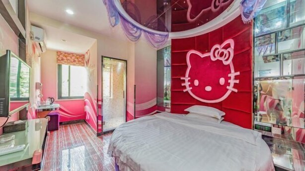 Et værelse med en stor seng, et sminkebord med spejl og en rød væg med Hello Kitty motiv.